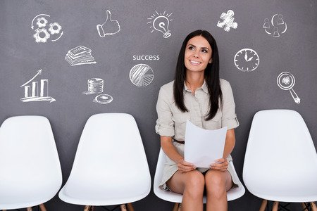 Confident young businesswoman holding paper while sitting on chair against grey backgroundの写真素材
