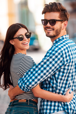 Enjoying time with each other. Happy young loving couple embracing and looking t camera while walking along the streetの写真素材