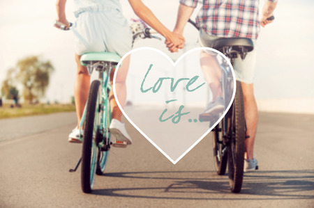 Love is... Rear view of young couple holding hands while riding on bicycles along the roadの写真素材