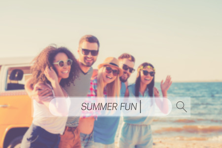 Summer fun. Group of cheerful young people embracing and looking at camera while walking along the beachの写真素材