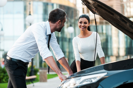 He is always ready to help. Two smiling young business people looking at each other while leaning at the opened vehicle hoodof the carの写真素材