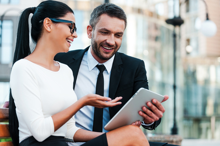 Keeping up with the latest news. Low angle view of cheerful young businesswoman pointing at digital tablet while her male colleague holding itの写真素材