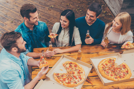 Enjoying time together. Top view of five happy young people holding bottles with beer and eating pizza while standing outdoors Enjoying time together. Top view of five happy young people holding bottles with beer and eating pizza while standing outdoors