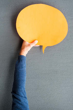 Speech bubble. Close-up of man stretching out empty speech bubble against grey backgroundの写真素材