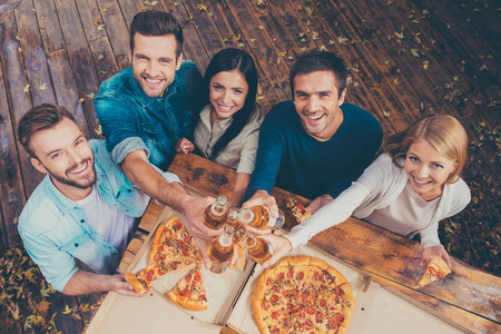 Celebrating that day. Top view of five happy young people clinking glasses with beer and looking at camera while standing outdoors Celebrating that day. Top view of five happy young people clinking glasses with beer and looking at camera while standing outdoors