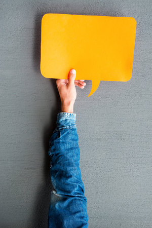 Write your thoughts. Close-up of man stretching out empty speech bubble against grey background