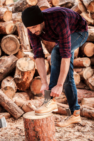 Getting ready to work. Full length of confident young forester adjusting his shoes while leaning at the logの写真素材