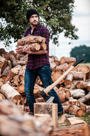 Lumberjack at work. Handsome young forester holding logs and looking away while standing outdoorsの写真素材