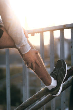 Never forget to stretch. Close-up of man stretching his leg before running while standing outdoorsの写真素材