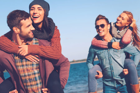 Carefree time with friends. Two beautiful young couples walking by the beach and smiling