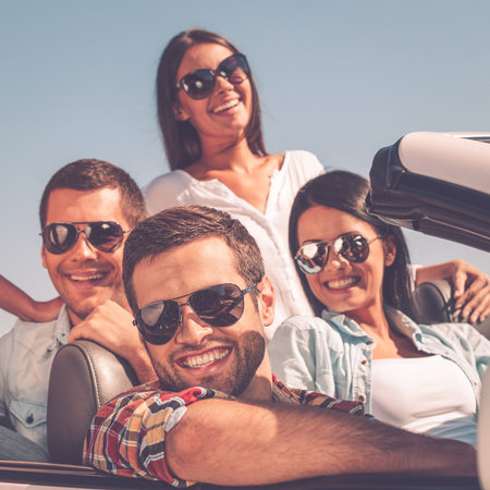 Enjoying time together. Group of young happy people enjoying road trip in their white convertible