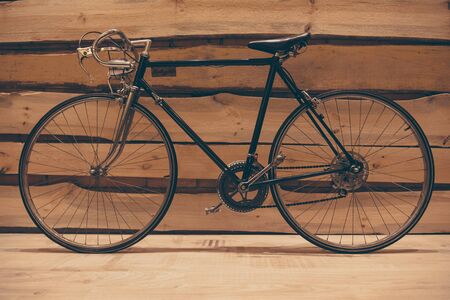 Retro styled bicycle. Close-up of retro styled bicycle standing against rough wooden wallの写真素材