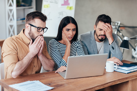 Oh no! Three frustrated young business people in smart casual wear looking at the laptop and expressing negativityの写真素材