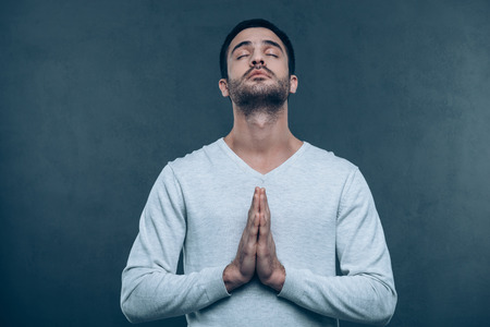 Man praying. Studio shot of handsome young man praying while holding hands clasped and keeping eyes closedの写真素材