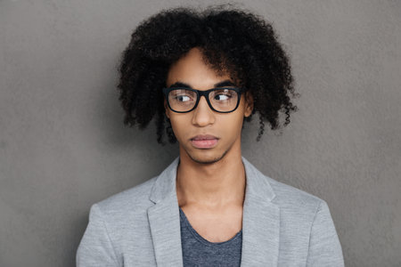 Lost in thoughts. Portrait of thoughtful young African man wearing glasses while standing against...