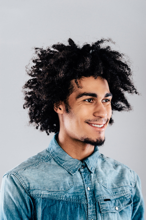 Cheerful and handsome.Portrait of handsome young African man looking away with smile while standing against grey backgroundの写真素材