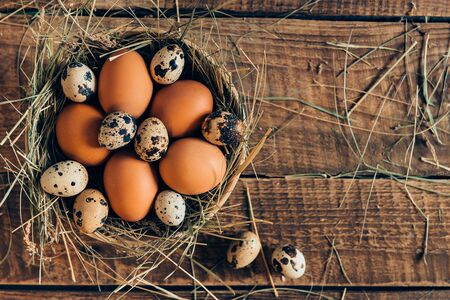 Fresh and organic eggs. Top view of brown eggs in bowl with hay lying on wooden rustic tableの写真素材