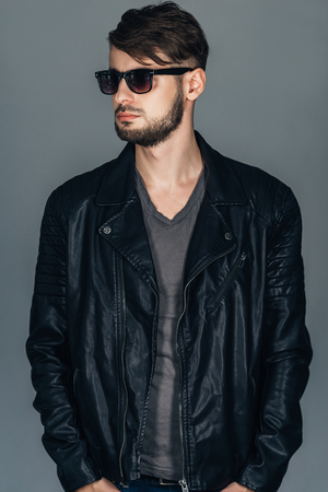 Black is a new black. Confident young man in sunglasses looking away while standing against grey backgroundの写真素材