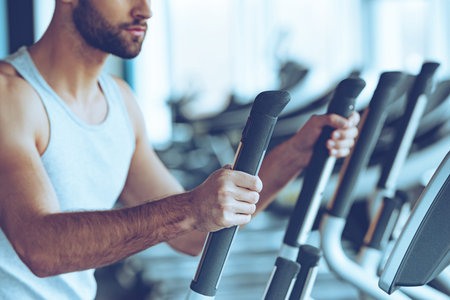 Working out. Side view close-up part of young man in sportswear working out on stepper at gym