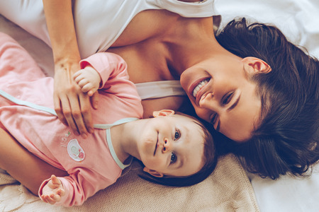 Best daughter ever. Top view of cheerful beautiful young woman lying in bed with her baby girlの写真素材