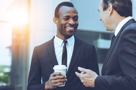 Coffee break. Two cheerful business men talking while one of them holding coffee cupの写真素材