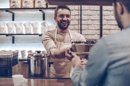Your cappuccino is ready! Rear view of barista passing coffee cups to his customer while standing at bar counterの写真素材