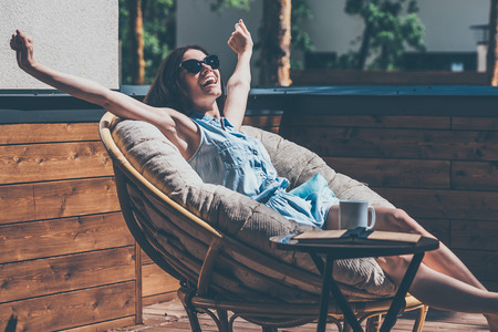 What a beautiful day! Beautiful young woman relaxing in a big comfortable chair on her outdoor house terraceの写真素材