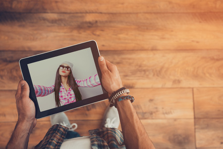 Distance in nothing for real love. Top view of man using video conference to communicate with his girlfriend while holding digital tablet and standing on the wooden floorの写真素材