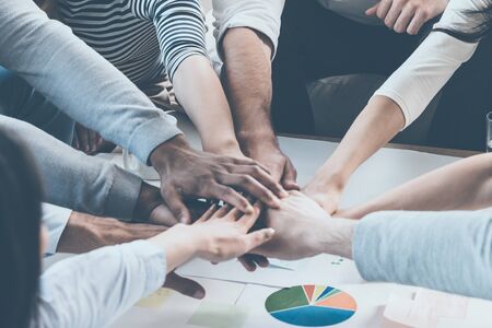 Unity concept. Close-up of people holding hands together while sitting around the deskの写真素材