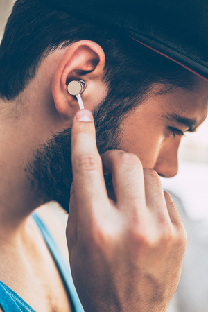 Enjoying his favorite music. Close-up of young man adjusting his headphones while standing outdoorsの写真素材