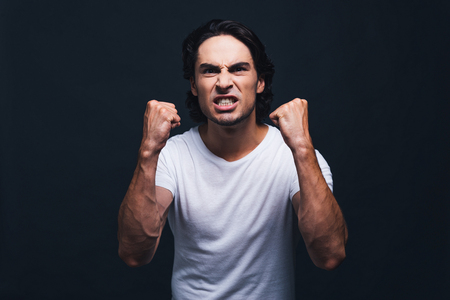 Feeling so angry now. Angry young man looking at camera and making a face while standing against grey backgroundの写真素材