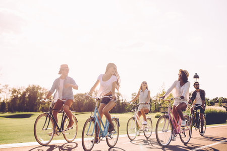 Best friends and road ahead. Group of young people riding bicycles along a road and looking happy