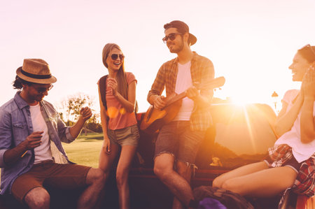 Enjoying road trip with friends. Group of young cheerful people dancing and playing guitar while...