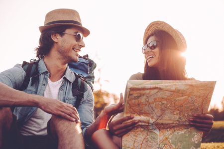 Finding their own way. Low angle view of beautiful young couple with backpacks examining map...