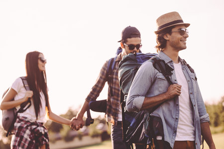 Summer hike with friends. Young people with backpacks walking together and looking happy