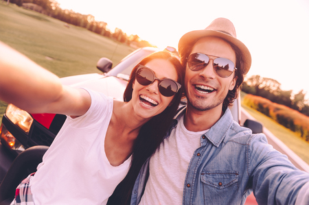 We love selfie! Beautiful young couple bonding to each other and leaning at their pick-up truck while making selfieの写真素材