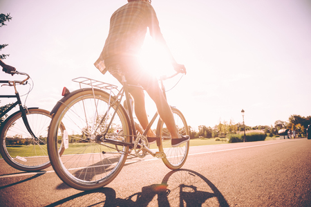 On the way to sunrise. Low angle view of young man riding bicycle together with his friends along the roadの写真素材