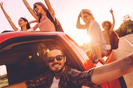 Capturing bright moments. Group of young cheerful people having fun in pick-up truck while driver making selfieの写真素材