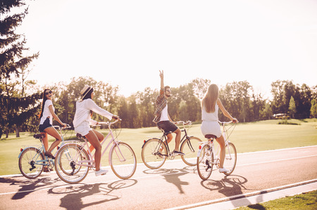 Spending great time together. Group of young people riding bicycles along a road and looking happyの写真素材