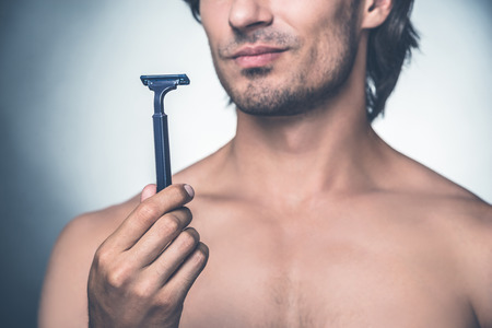 Time for new razor. Close-up young shirtless man holding razor and expressing negativity while standing against grey backgroundの写真素材