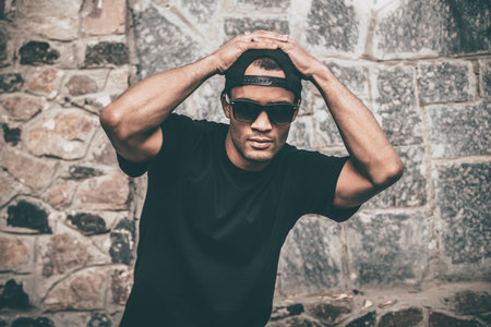 Young and cool. Handsome young African man in casual clothes holding hands on cap and looking at...