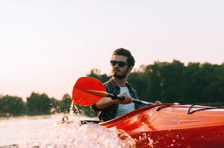 Feeling confident on water. Confident young man kayaking on lake with sunset in the background