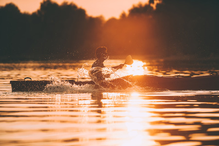 Meeting sunset on kayak. Side view of man kayaking on river with sunset in the backgroundの写真素材