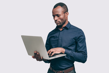 Businessman at work. Handsome young African man working on laptop while standing against grey backgroundの写真素材
