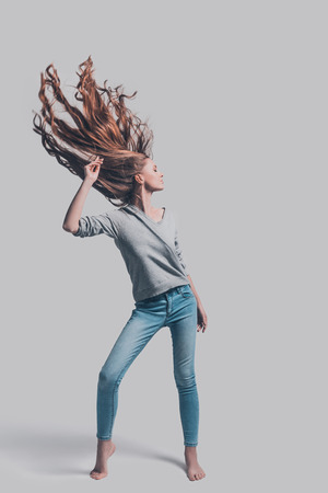 Hair like fire. Full length studio shot of attractive young woman with tousled hair posing against grey backgroundの写真素材