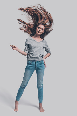 Beauty in motion. Full length studio shot of attractive young woman with tousled hair posing against grey backgroundの写真素材