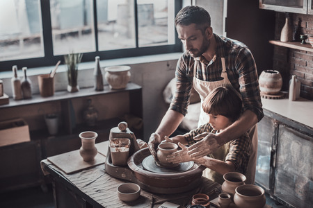 Creating something great together. Top view of confident young man and little boy making ceramic pot on the pottery classの写真素材