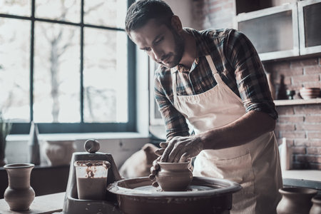 Concentrated at work. Confident young man making ceramic pot on the pottery wheelの写真素材