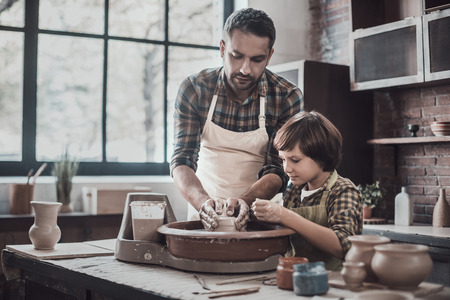 Pottering with son. Confident young man and little boy making ceramic pot on the pottery classの写真素材