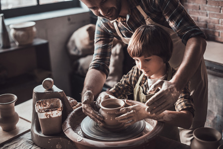 Learning new skill from potter. Top view of cheerful young man and little boy making ceramic pot on the pottery classの写真素材